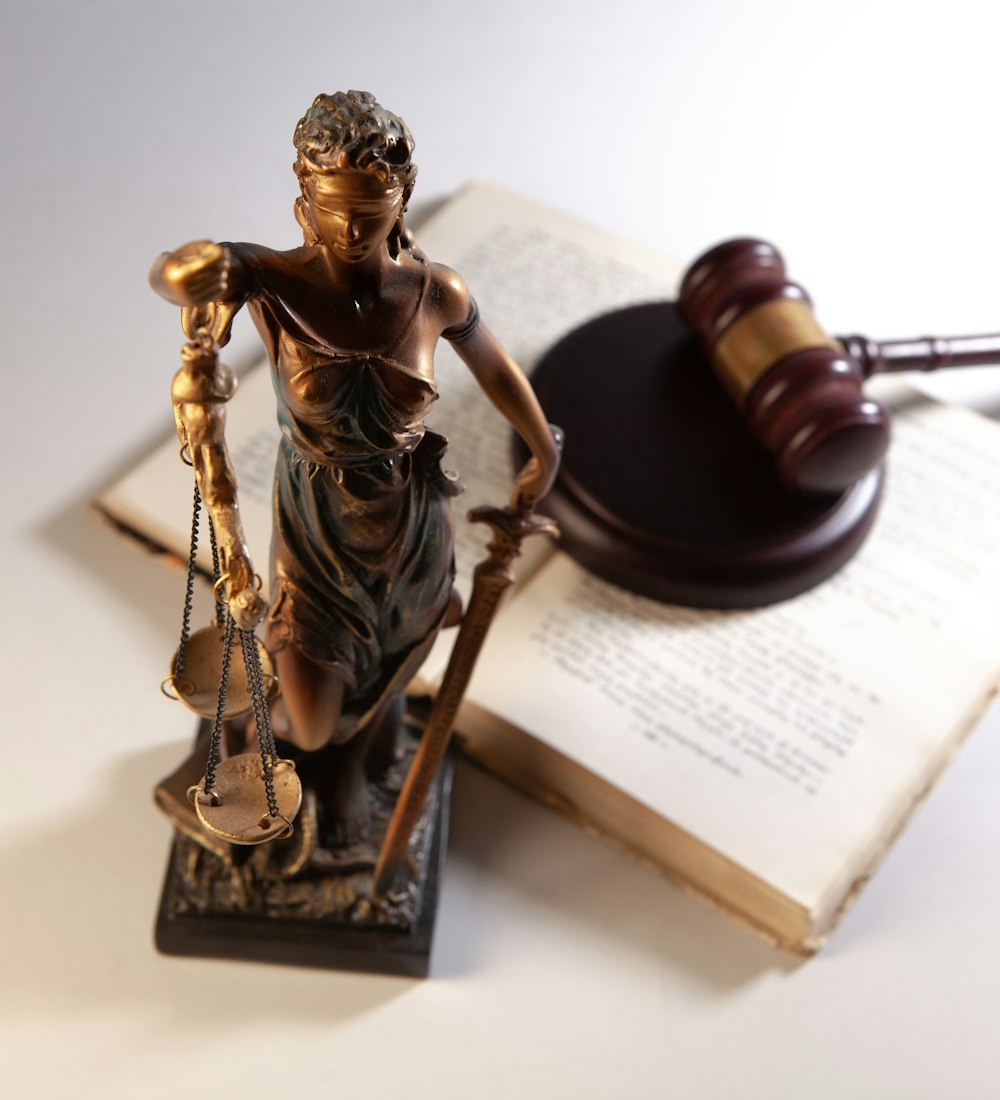Small statue of Lady Justice beside a gavel and an open law book